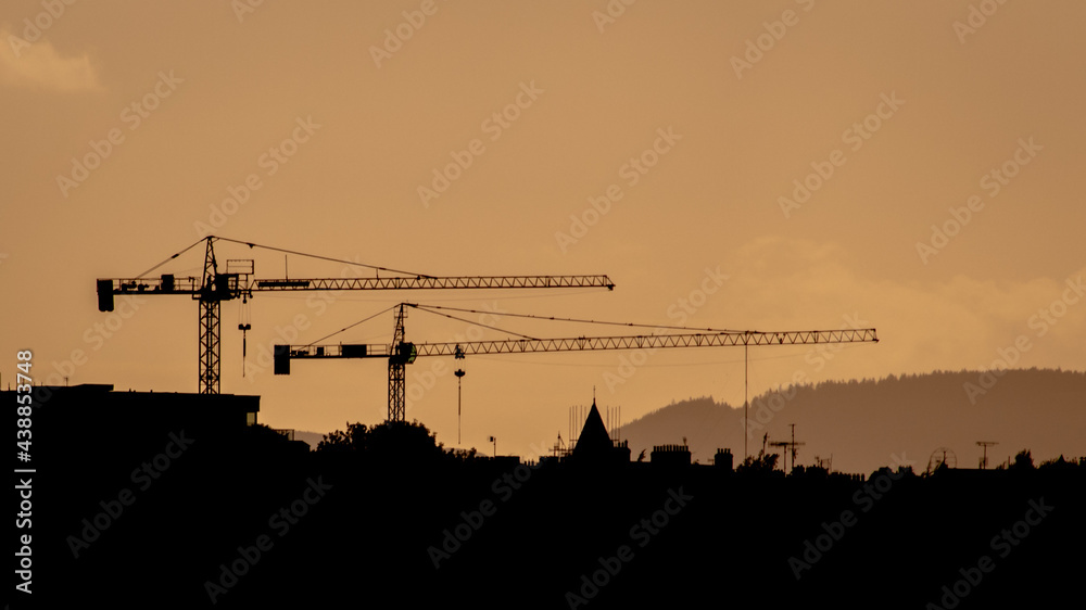 Naklejka premium Two Construction Cranes Silhouette at Sunset on Dublin Sky