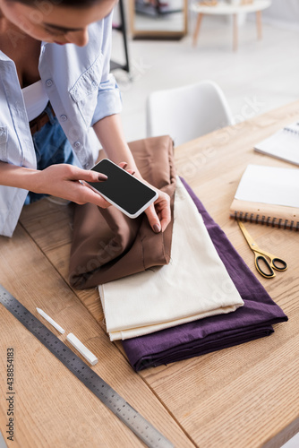 Seamstress using smartphone near fabric, scissors and ruler on table