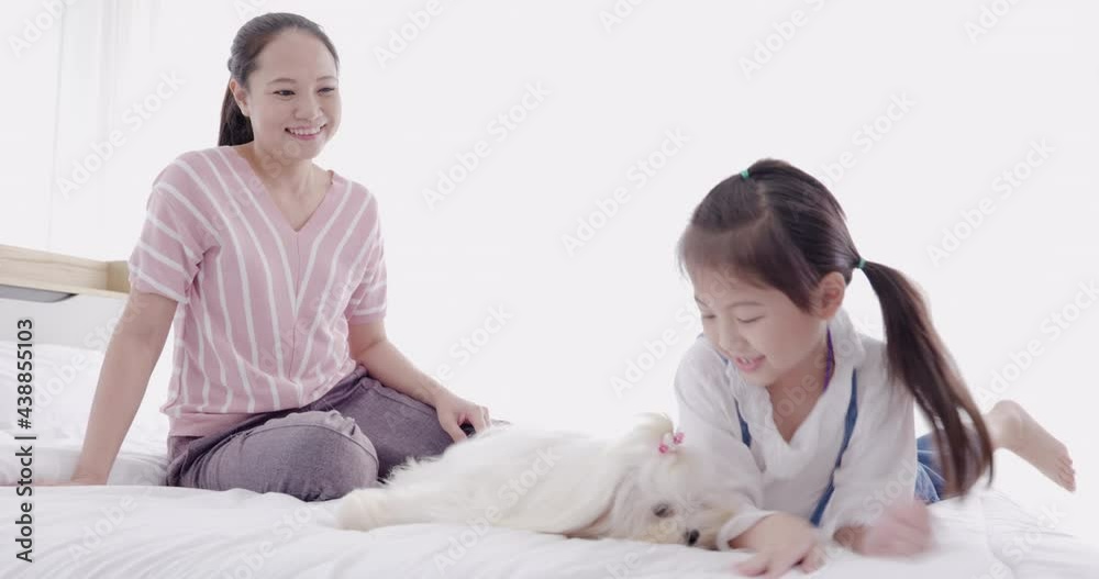 mother and daughter playing with white dog on bed 4
