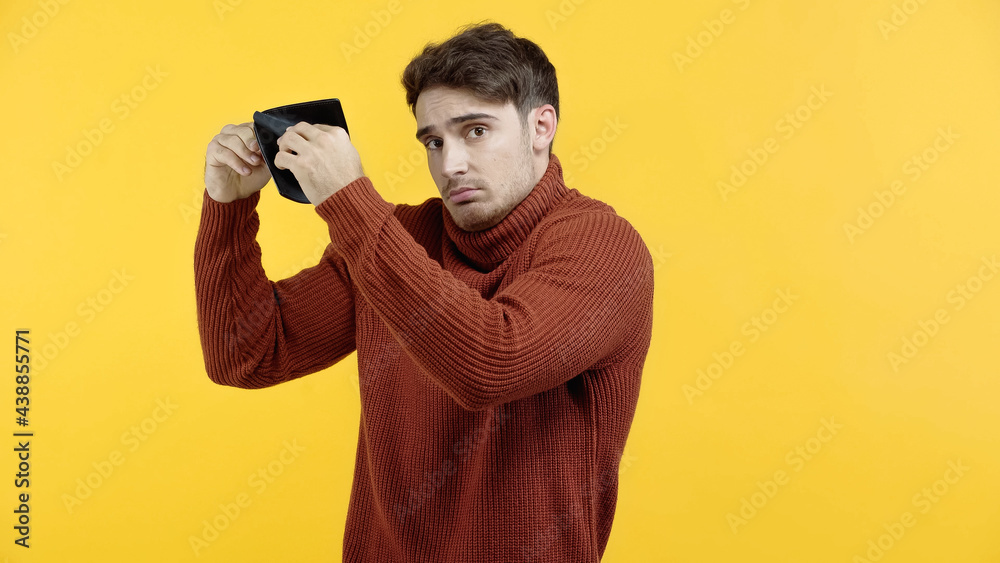 Displeased man in sweater holding empty wallet isolated on yellow Displeased man in sweater holding empty wallet isolated on yellow