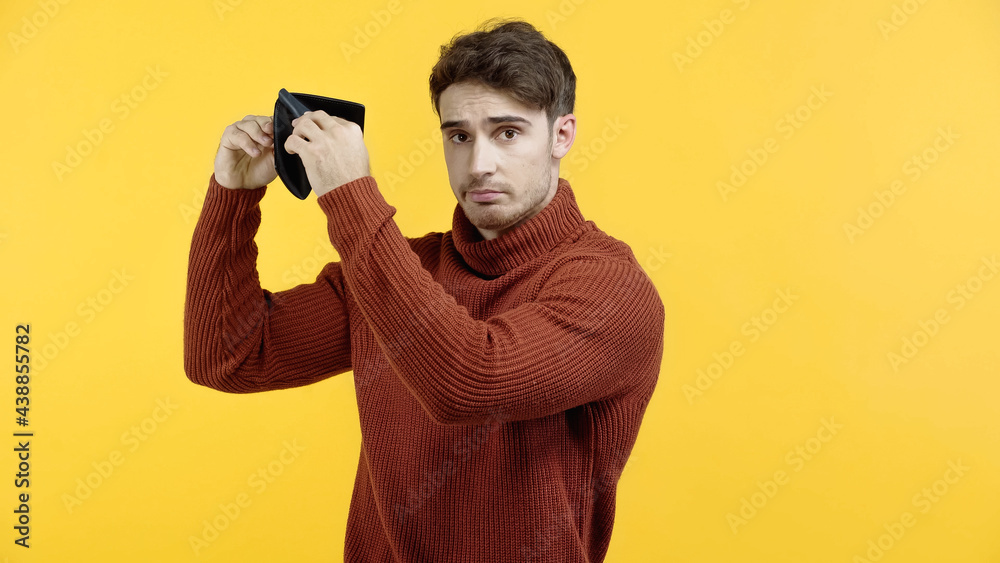 Upset man holding empty wallet isolated on yellow Upset man holding empty wallet isolated on yellow