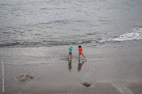 playa con el mar en calma y dos chicas mojando los pies con las olas photo