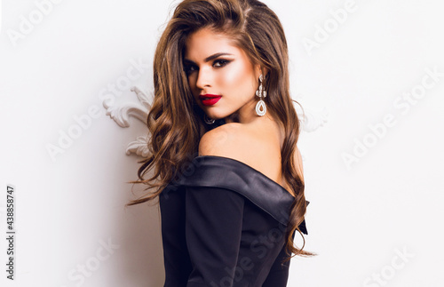 фотографія Beautiful stunning  woman with red full lips, smokey eyes make up , shining perfect  wavy hairs in  elegant casual black dress   posing on white background