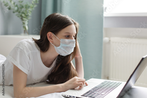 Teenager girl with face mask studying online at home
