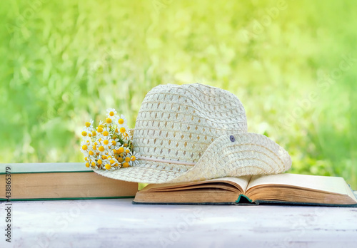 Fototapeta Naklejka Na Ścianę i Meble -  Chamomile flowers, book and summer hat in sunny garden, natural background. relax time, summer season concept. Rustic composition