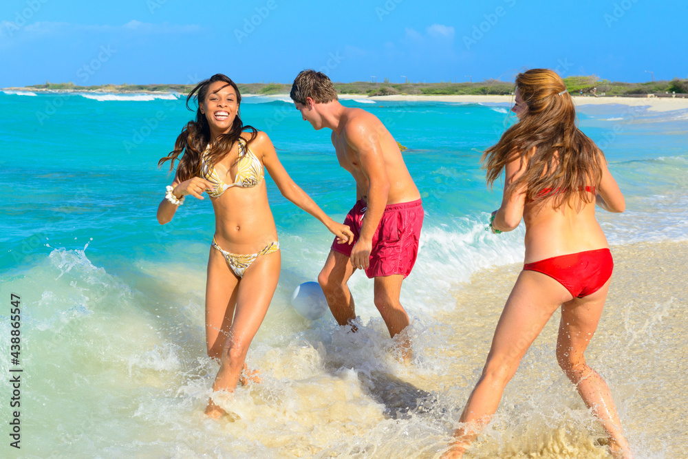 Three young beautiful people, couple, playing with a ball, running on the beach at the seashore, interracial, black Three young beautiful people, couple, playing with a ball, running on the beach at the seashore, interracial, black