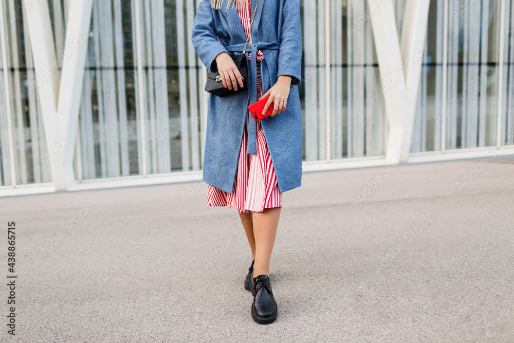 Happy brunette woman in blue coat and red dress walking along modern street Happy brunette woman in blue coat and red dress walking along modern street
