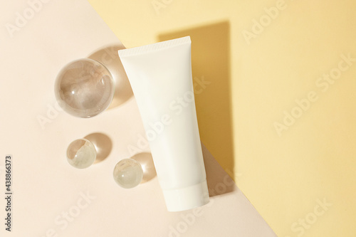 Top view of the blank cosmetics tube on the dual pastel background.Glass sphers near it,concept of the cleanness and clarity.Cosmetic mockup with copy space. photo