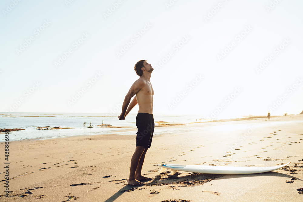 Fit surfer stretching arms on sandy beach