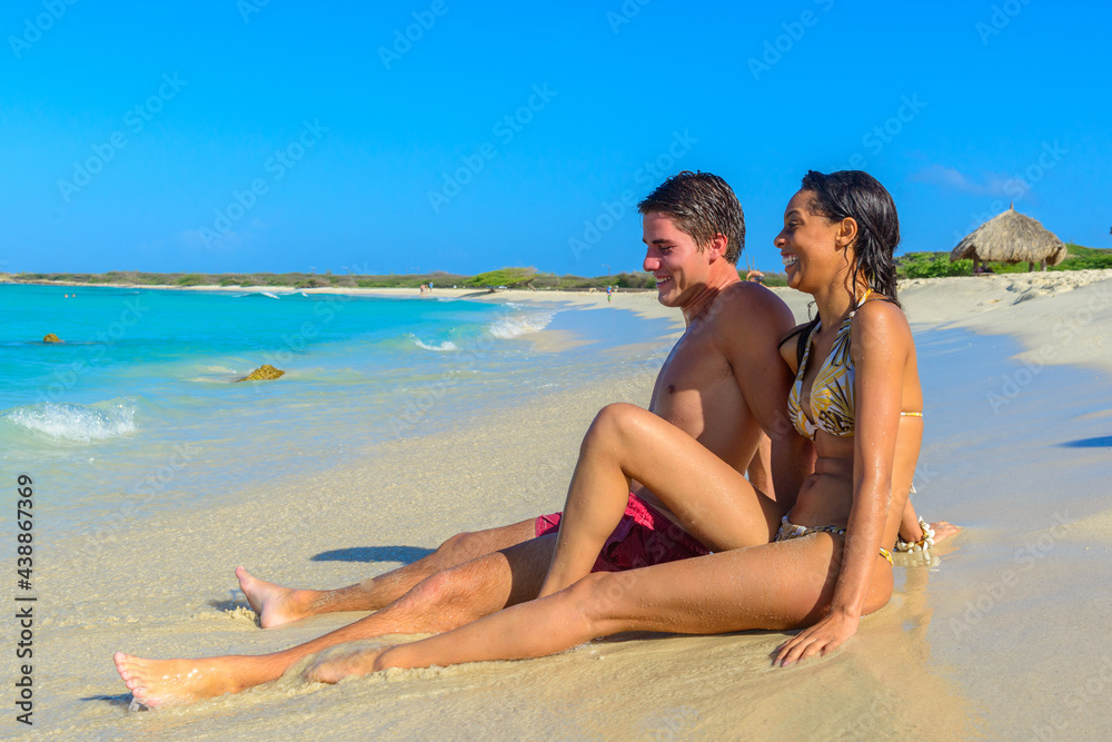 Two young beautiful people sitting on the beach at the seashore, interracial, black