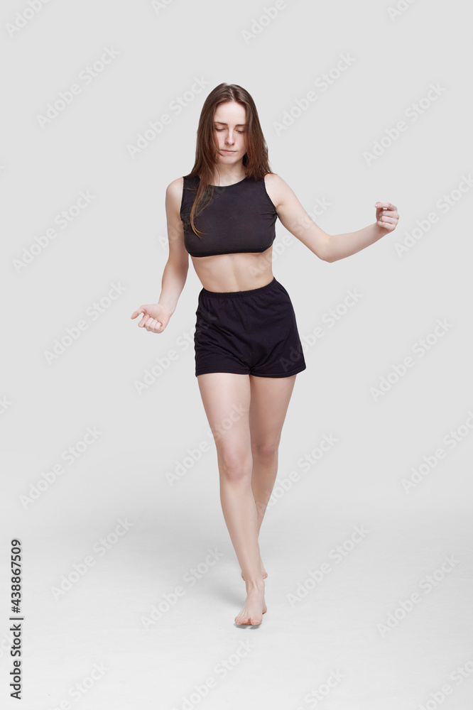 Young slim athletic girl, with long hair, in a black top and shorts, in the studio on a white background Young slim athletic girl, with long hair, in a black top and shorts, in the studio on a white background