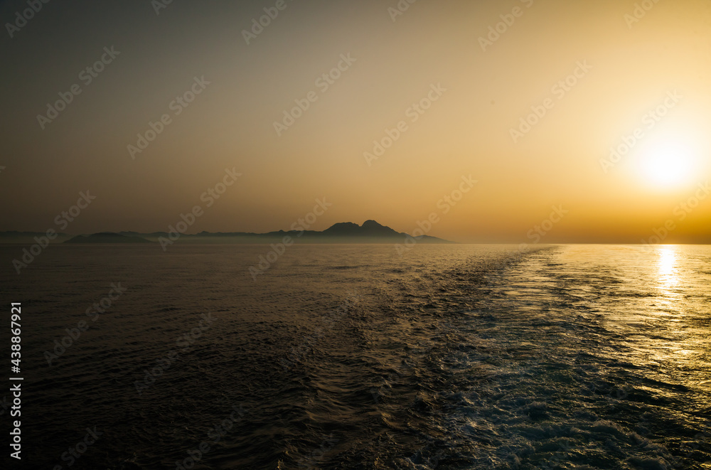 Sunset on the sea, mountains in the distance on the horizon and the trail of the movement of the ship on the water.