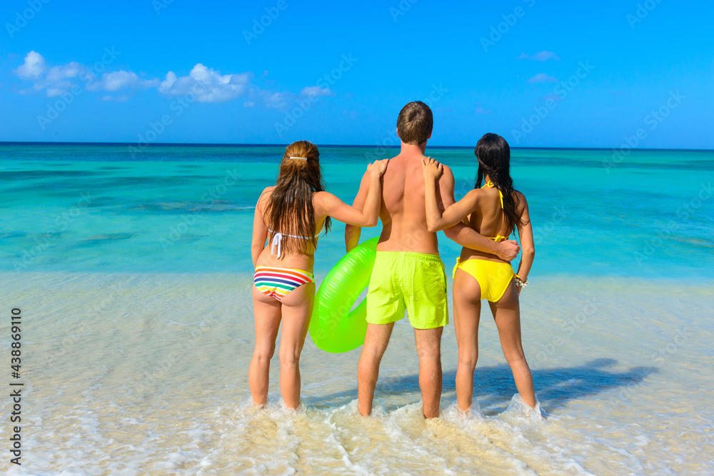 Three young beautiful people standing on the beach with a lifesaver, looking towards the horizon, interracial, black