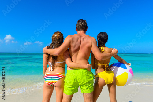 Three young beautiful people standing on the beach with a beach ball looking toward the horizon, interracial, black