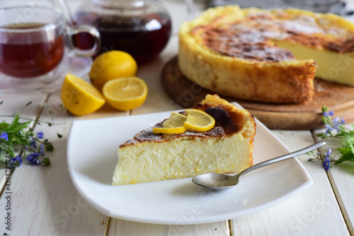 Sweet snack  a slice of cheese pie with lemon on a nice plate  a cheese pie and a cup of tea on a white table