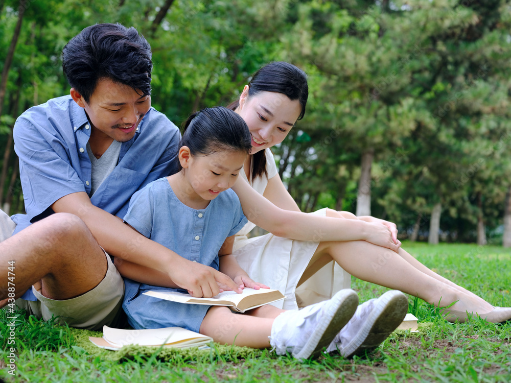 A happy family of three is reading outdoors A happy family of three is reading outdoors
