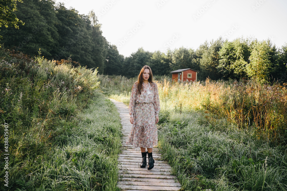 beautiful woman in a summer dress and boots walks along a wooden path.