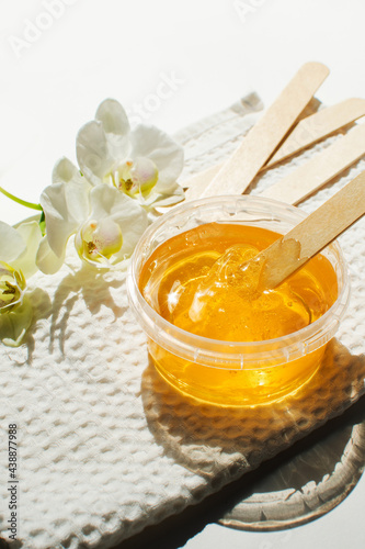 Sugar paste or wax honey in a transparent jar and white orchid on a white background. Sugaring. Depilation and beauty concept. Waxing.