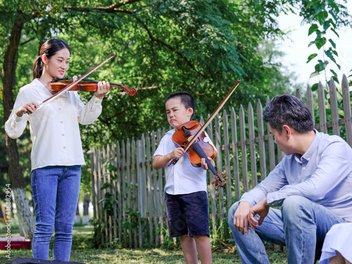 Happy family of three playing violin in the park