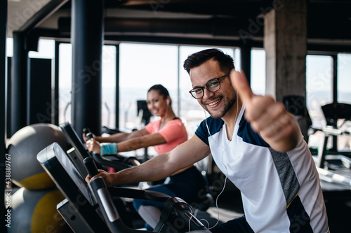 Young and attractive woman and man biking in the fitness gym. They exercising legs and doing cardio workout while riding cycling machines.