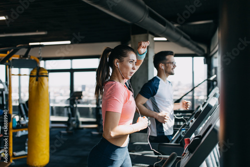 Young fit man and woman running on treadmill in modern fitness gym.