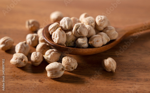 Dried chickpeas and a wooden spoon placed on a wooden background.