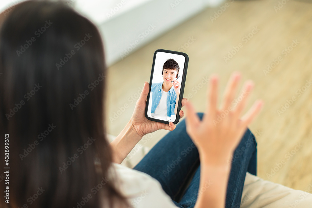 Young woman sitting on sofa at home, holding mobile phone, making video call, discussing with company colleagues in telecommuting