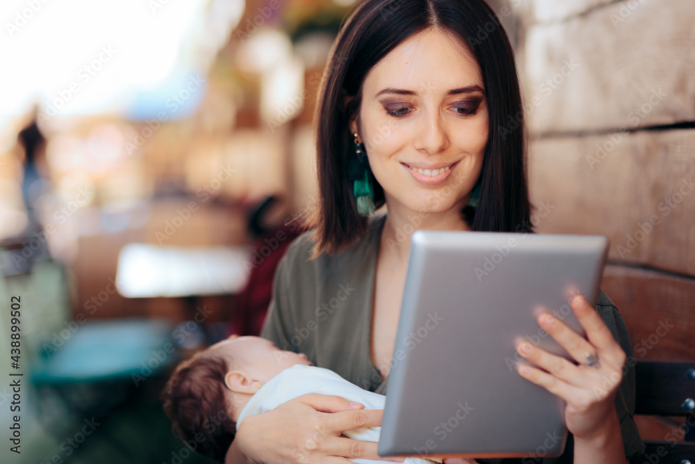 Happy Working Mom Holding Sleeping Baby and Pc Tablet in a Restaurant Happy Working Mom Holding Sleeping Baby and Pc Tablet in a Restaurant
