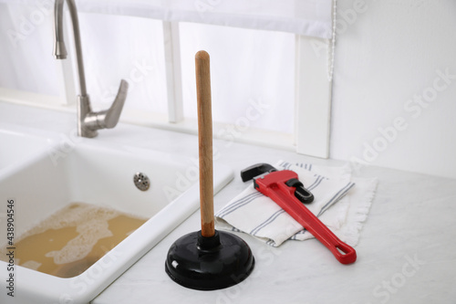 Plunger, pipe wrench and towel on kitchen counter near clogged sink
