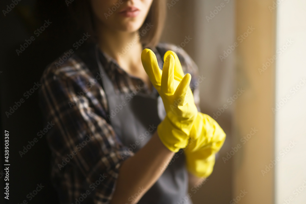 A young girl in a plaid shirt and apron puts yellow rubber gloves on ...