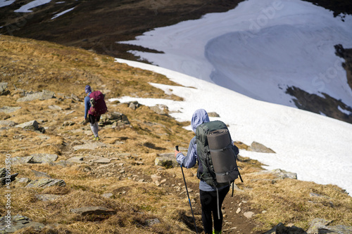 Two young hikers walk the mountains with trekking poles, backpacks and other tourist equipment. Girls climb in the early spring in the national park, make a walk surrounded by beautiful landscape. photo