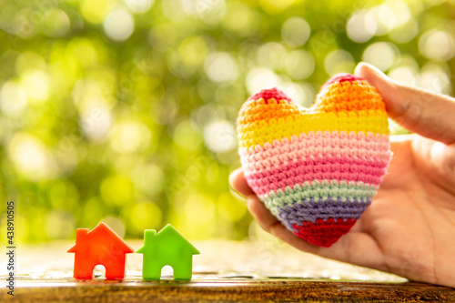 Hand are hold rainbow heart and home model.Give love to the family for happiness..Have background in garden and light of sun.