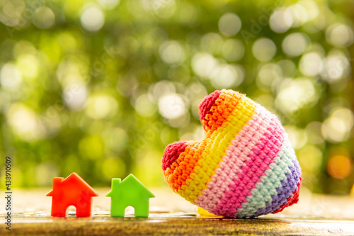 Hand are hold rainbow heart and home model.Give love to the family for happiness..Have background in garden and light of sun.