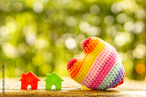 Hand are hold rainbow heart and home model.Give love to the family for happiness..Have background in garden and light of sun.