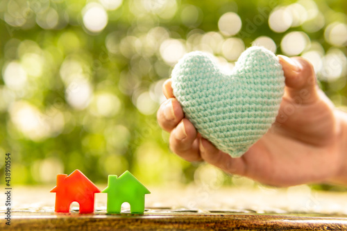 Hand are hold rainbow heart and home model.Give love to the family for happiness..Have background in garden and light of sun.