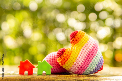 Hand are hold rainbow heart and home model.Give love to the family for happiness..Have background in garden and light of sun.