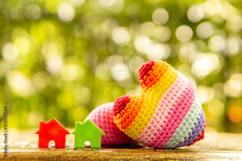 Hand are hold rainbow heart and home model.Give love to the family for happiness..Have background in garden and light of sun.