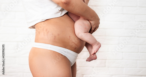 The belly of a woman after the birth of a child. Baby's legs on a woman's stomach on a white background