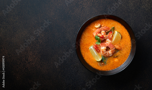 Tom Yum kung Spicy Thai soup with shrimp in a black bowl on a dark stone background, top view, copy space photo