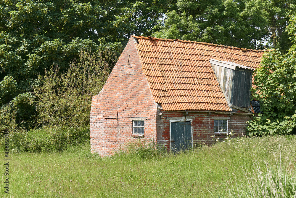 Fototapeta premium Old decaying shed with red bricks and orange tiles near Ferwert in The Netherlands. 