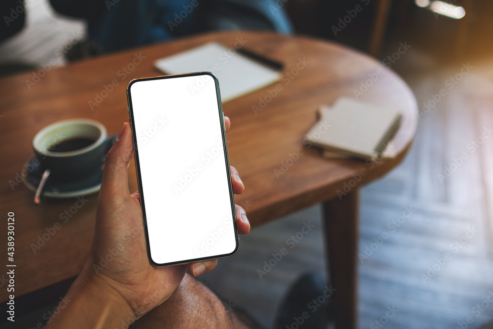 Mockup image of a man holding black mobile phone with blank white screen in cafe Mockup image of a man holding black mobile phone with blank white screen in cafe