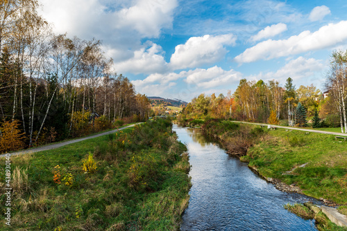 Autumn scenery with river, footpath and narrow road, colorful trees and smaller hills on the background near Brenna village in Poland photo