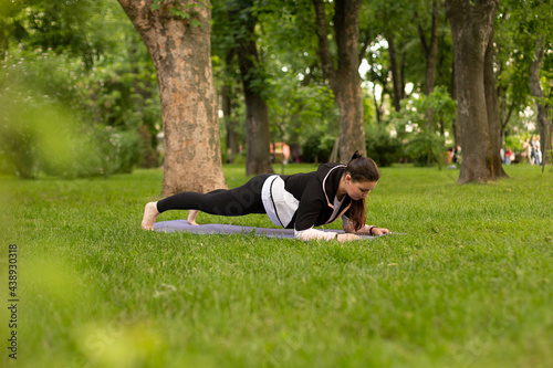 woman doing sports, shows exercise from pilates. practices yoga in the park on a green grass.
