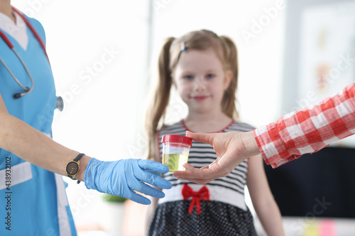 Mother giving doctor jar of urine analysis in front of little girl closeup photo