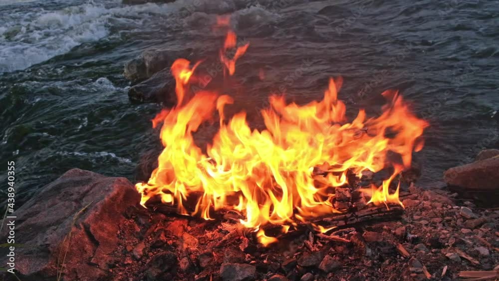 Slow Motion Video Burning Bonfire against Background Flowing River. Slow Motion Video Burning Bonfire against Background Flowing River.