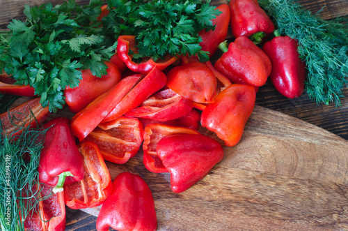 Raw red bell pepper, chopped in half and parsley on a wooden background.