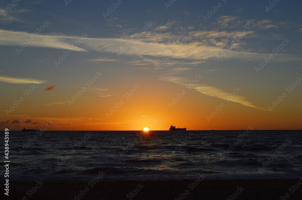 Beautiful Orange Sun rising above the sea level on Fort Lauderdale Beach with fishing boat far away