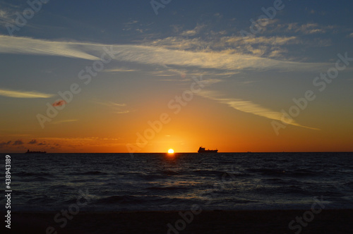 Beautiful Orange Sun rising above the sea level on Fort Lauderdale Beach with fishing boat far away