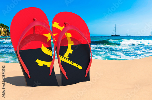Flip flops with Angolan flag on the beach. Angola resorts, vacation, tours, travel packages concept. 3D rendering