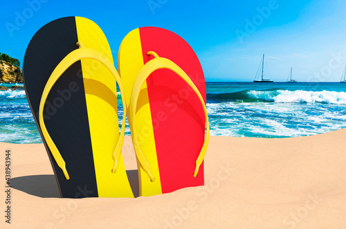 Flip flops with Belgian flag on the beach. Belgium resorts, vacation, tours, travel packages concept. 3D rendering